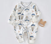 A white baby jumpsuit with colorful balloon prints and long sleeves, accompanied by a teething ring.